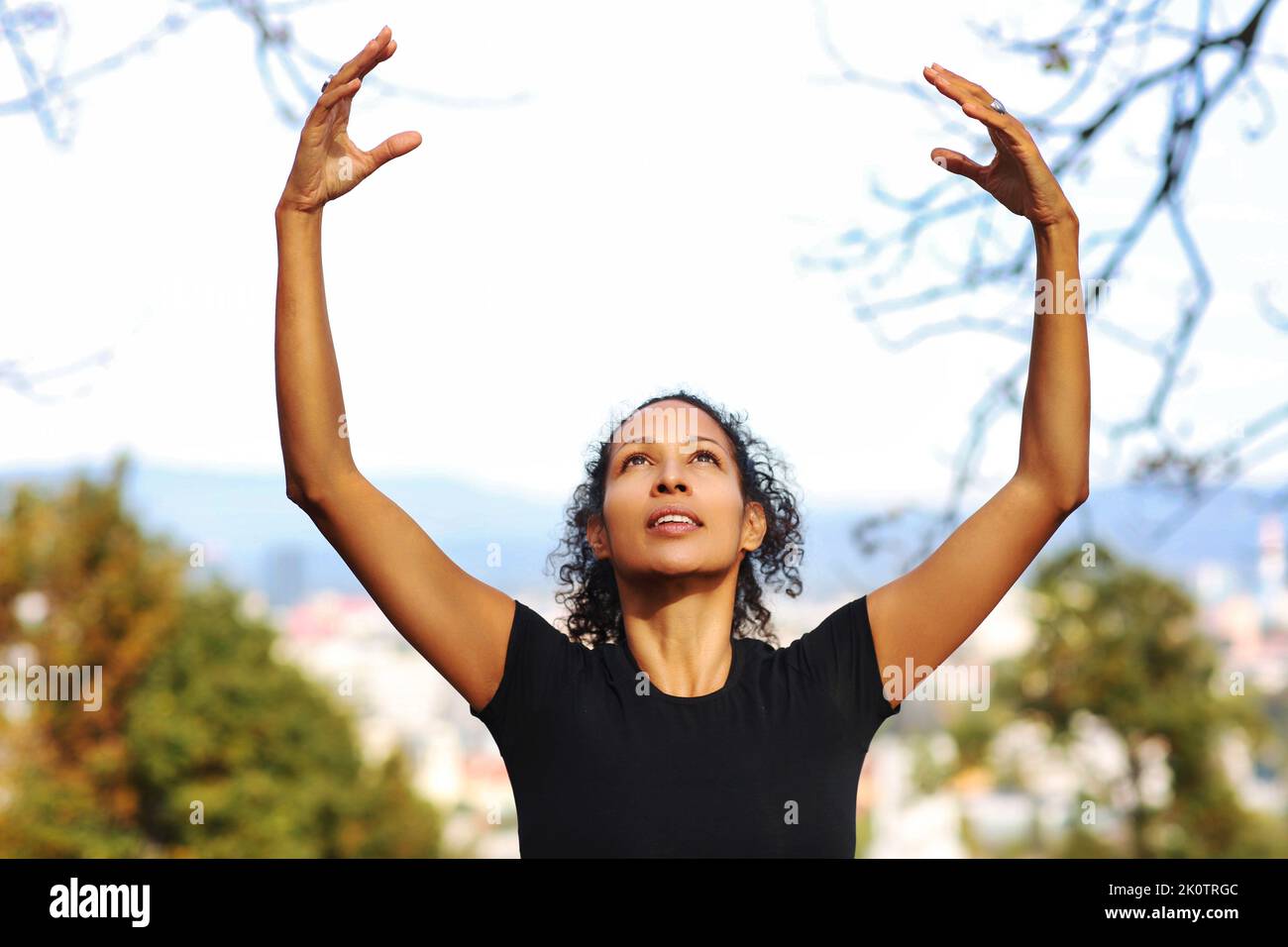 woman outdoors, arms raised curly hair sportswear Stock Photo