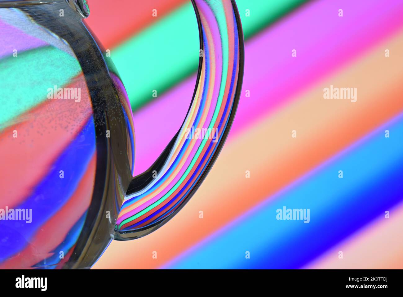 Ilusión óptica creada mediante la refracción de la luz con un recipiente de cristal lleno de agua y líneas diagonales de colores Stock Photo