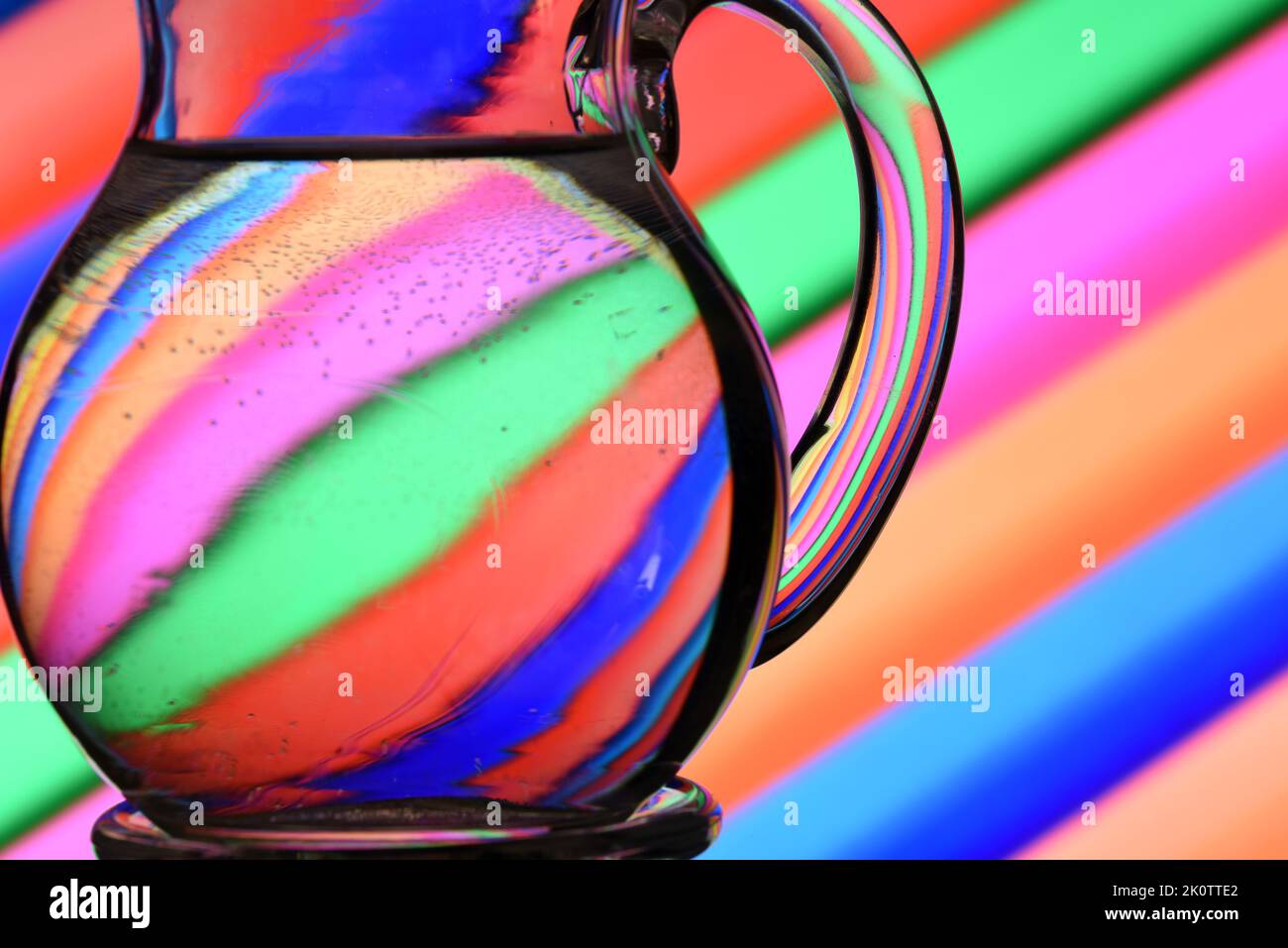 Ilusión óptica creada mediante la refracción de la luz con un recipiente de cristal lleno de agua y líneas diagonales de colores Stock Photo