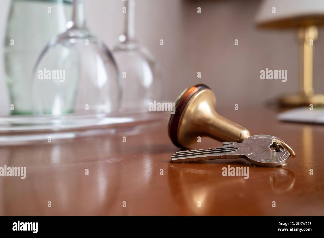 Key with a key fob from the hotel room lies on the table, against a blurred background of clean wine glasses and a lamp. Close-up. Stock Photo