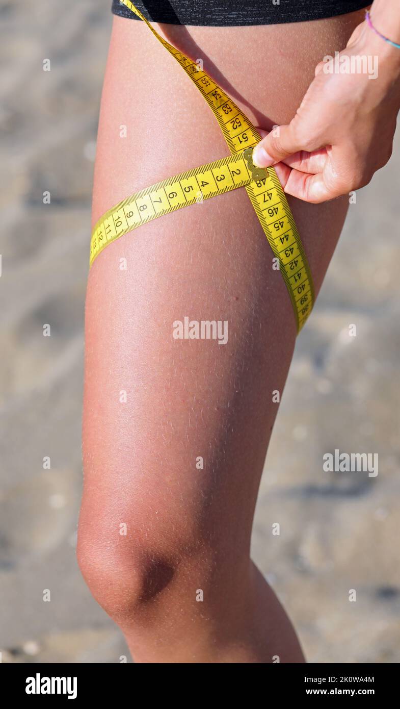 skinny girl measures her waistline after the weight loss diet with a yellow  flexible measuring tape Stock Photo