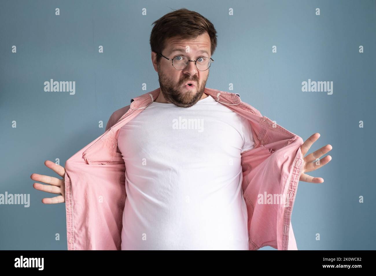 Overweight man opens shirt and shows his excess belly fat, with a strange expression on face. Healthy lifestyle concept. Stock Photo