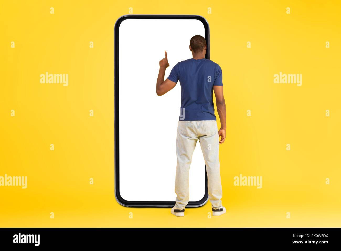 African Man Using Large Smartphone Over Yellow Background, Back View Stock Photo