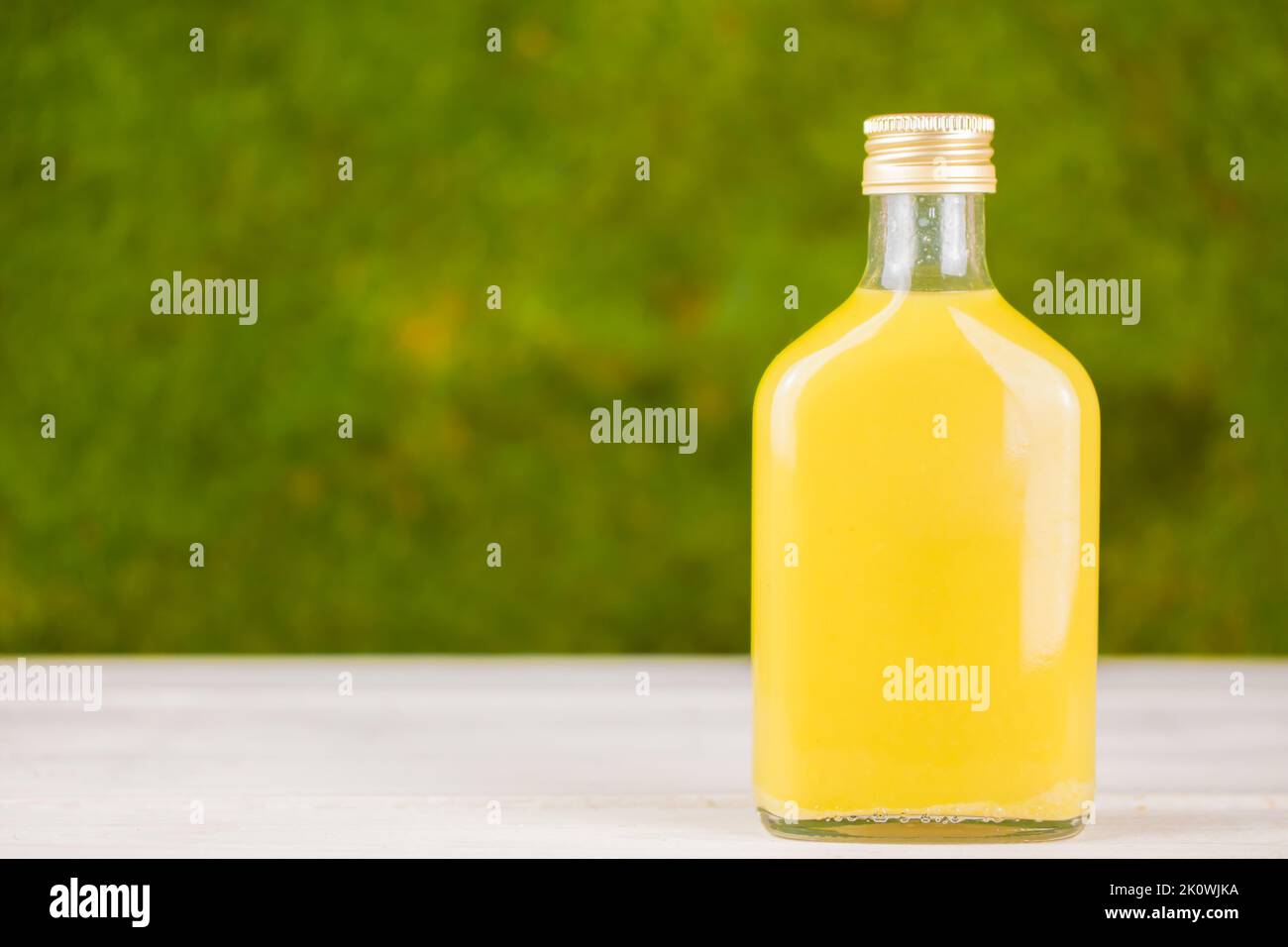 Yellow drink - homemade ginger shot, citrus juice or lemonade in glass bottle. Green background. Immunity boosting healthy drink. Copy space for text. Stock Photo