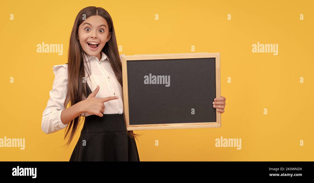 surprised child in uniform pointing finger on school blackboard for copy space, advertisement Stock Photo