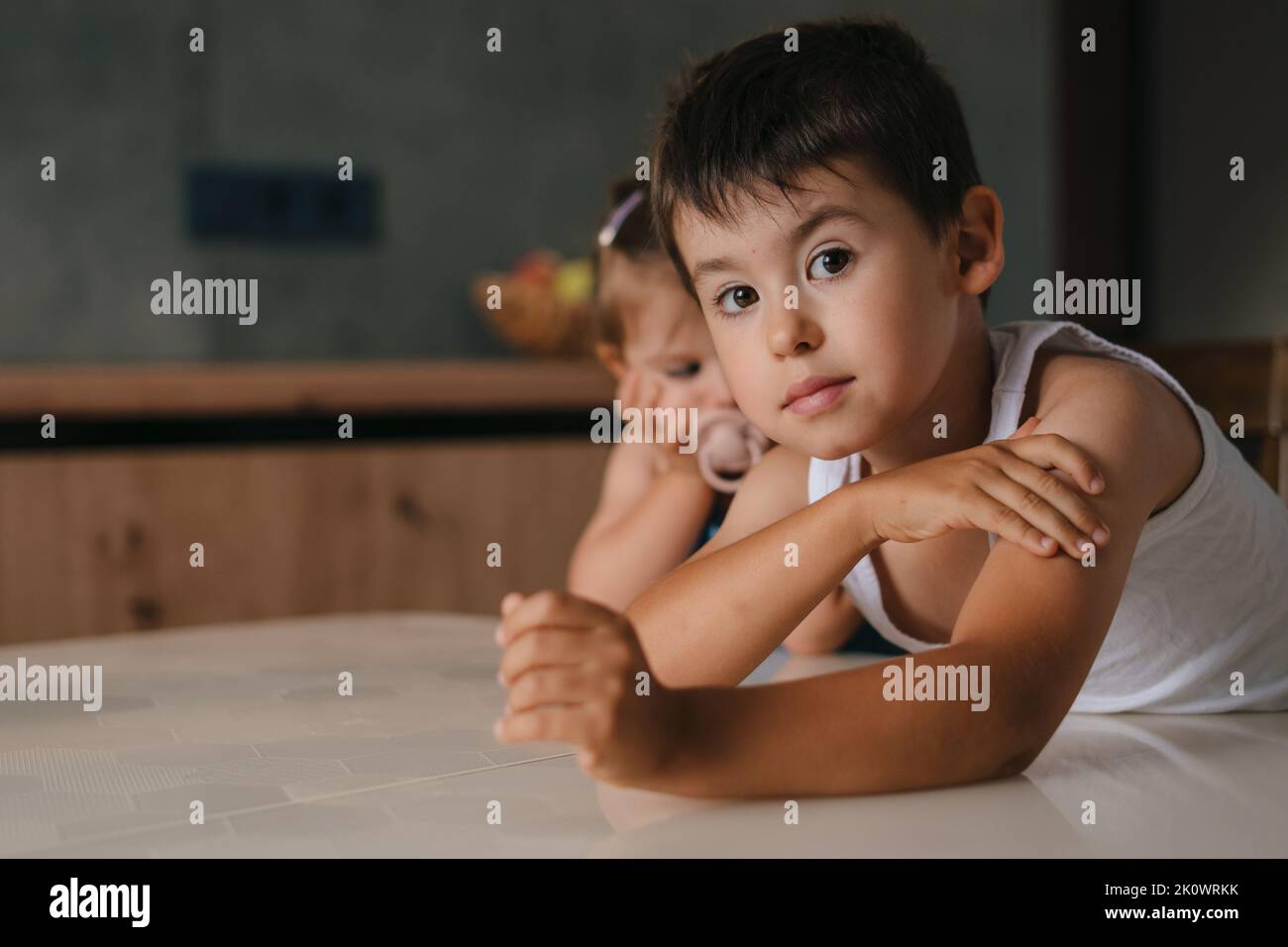 Cute small little boy with his baby sister waiting for food, enjoy happy childhood at home. Waiting for dinner or breakfast, family enjoying weekend Stock Photo