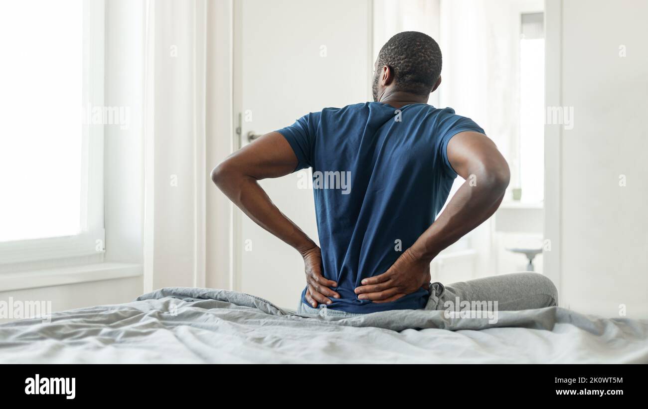 African Man Having Pain Touching Lower Back Sitting In Bedroom Stock