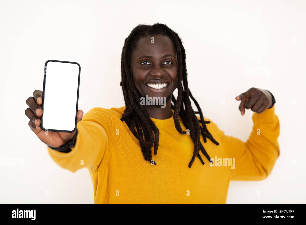 Online Offer. Cheerful Black Guy Pointing At Blank Smartphone In His Hand Stock Photo