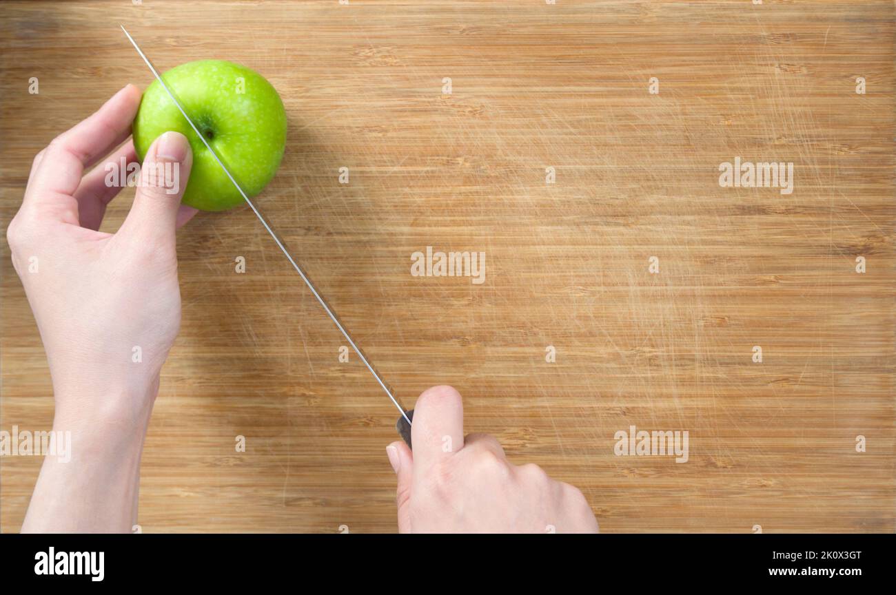 Closeup hand holding knife cutting green apple on a wooden chop board ...