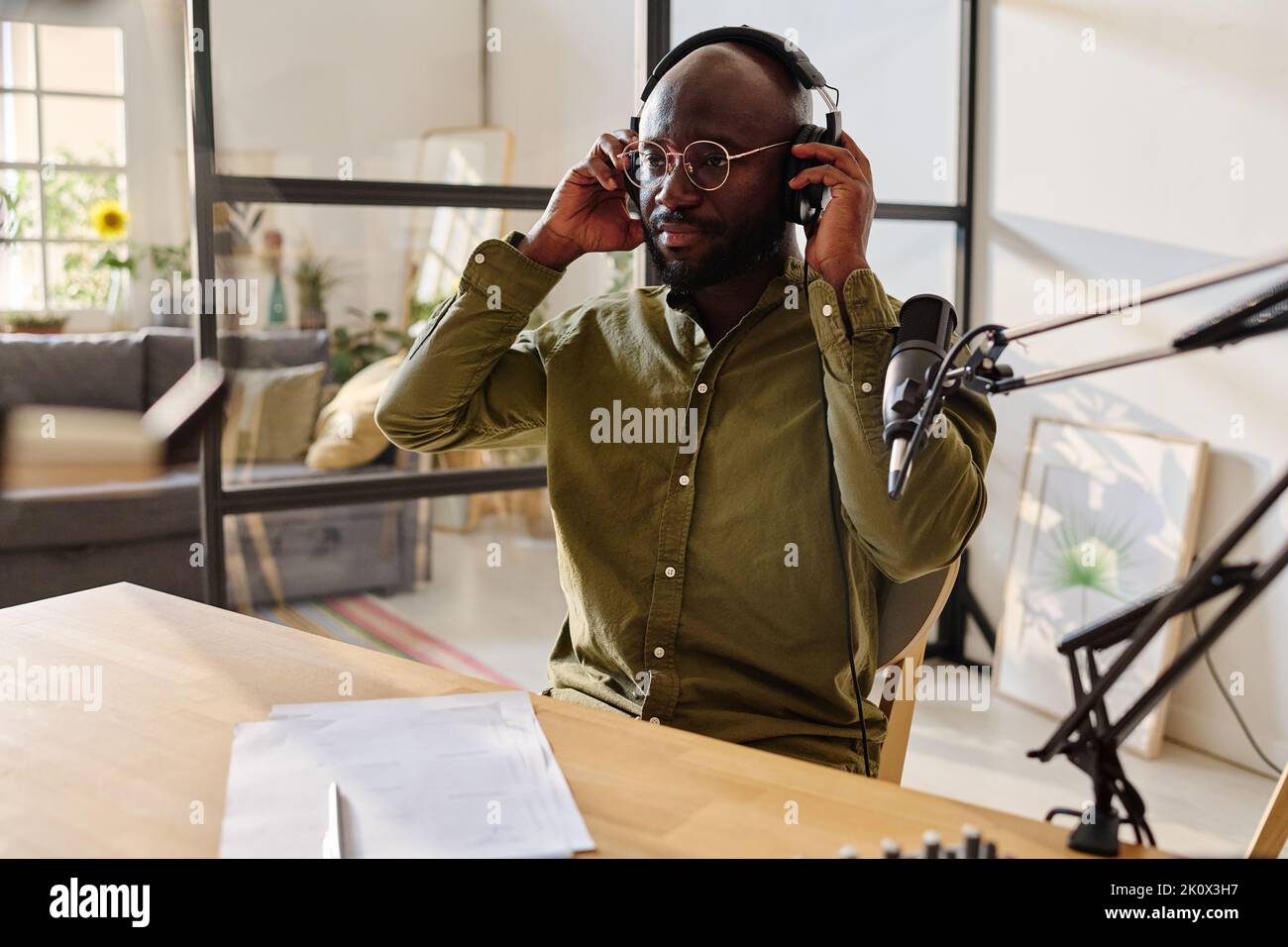 Young African American man putting on headphones while preparing for recording audio file with his speculations on topical subject Stock Photo