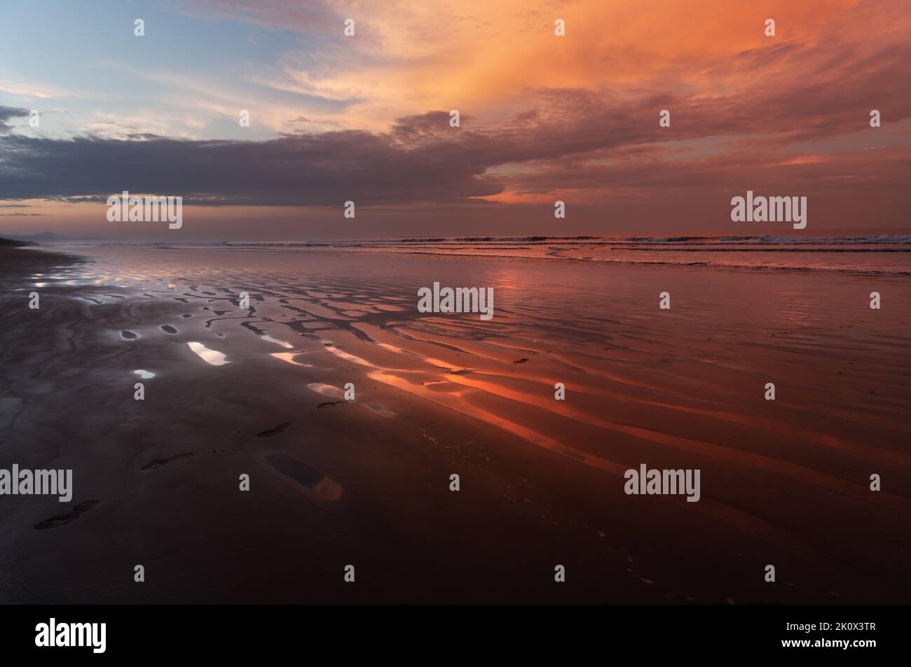 Vivid dawn colors at a tropical beach and sky clouds reflection on wet sand, shown in Chiriqui, Panama. Stock Photo