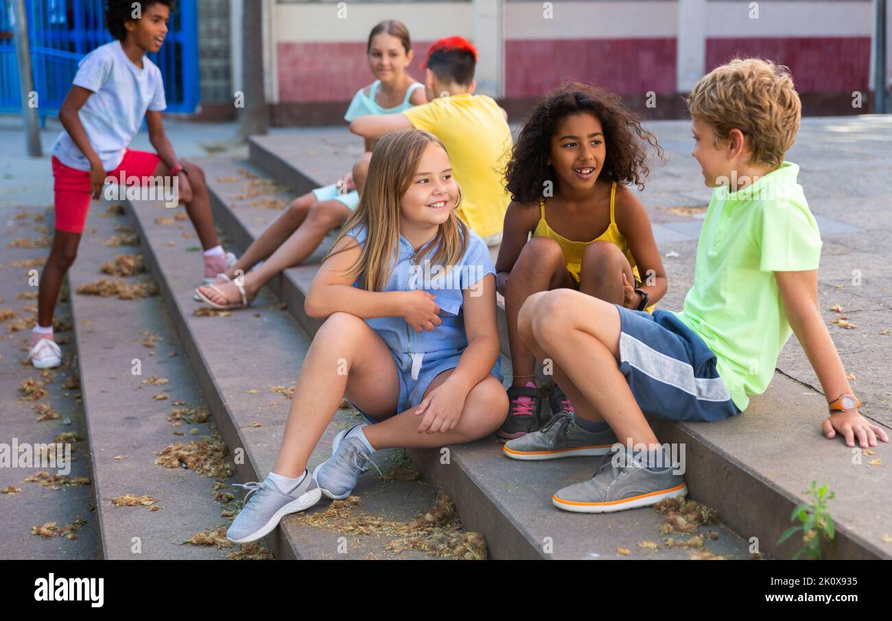 Happy tweenagers friends sitting on steps outdoors and chatting Stock Photo