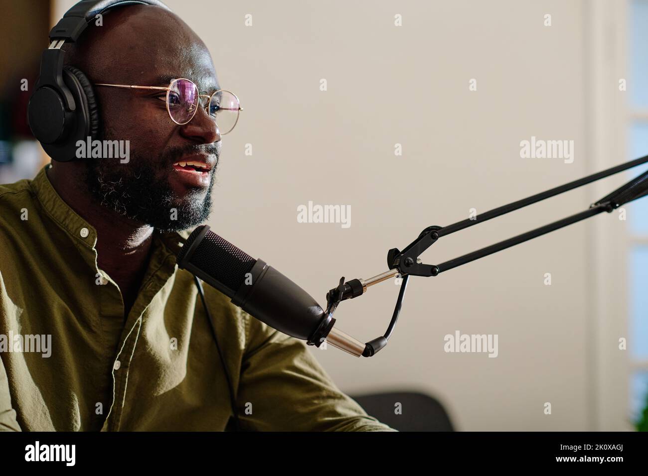 Young modern male host in headphones sitting in front of microphone and speculating about topical subject while recording audio file Stock Photo