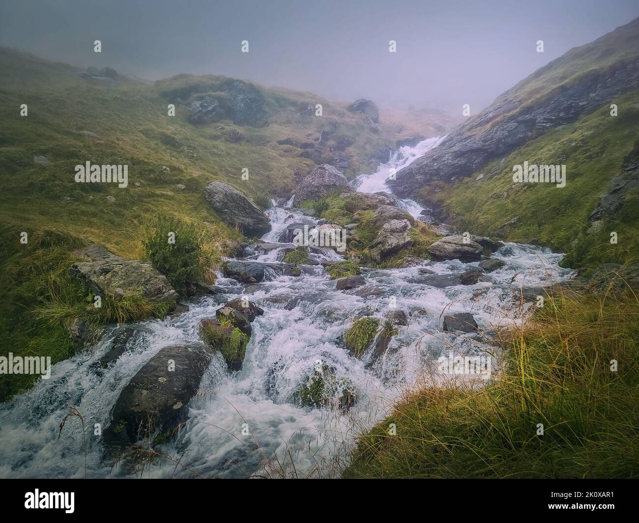 Fast stream flowing across a rocky valley in Fagaras Mountains. River with waterfalls and dense mist landscape Stock Photo