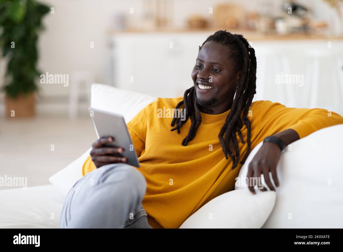 Smiling black man watching videos on digital tablet while resting on couch Stock Photo