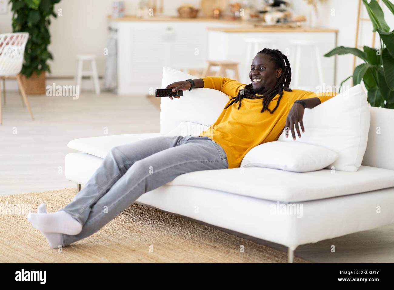Weekend Pastime. Cheerful Black Guy Sitting On Couch And Watching Tv Stock Photo