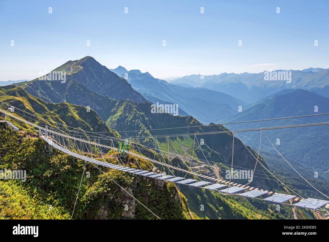 Suspension bridge with transparent floors is suspended in the mountains over an abyss. Away against the backdrop of the peak of the peak of the mounta Stock Photo