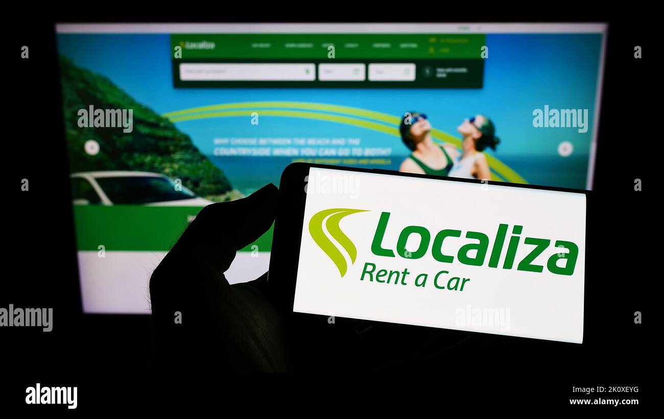 Person holding smartphone with logo of Brazilian company Localiza Rent a Car S.A. on screen in front of website. Focus on phone display. Stock Photo