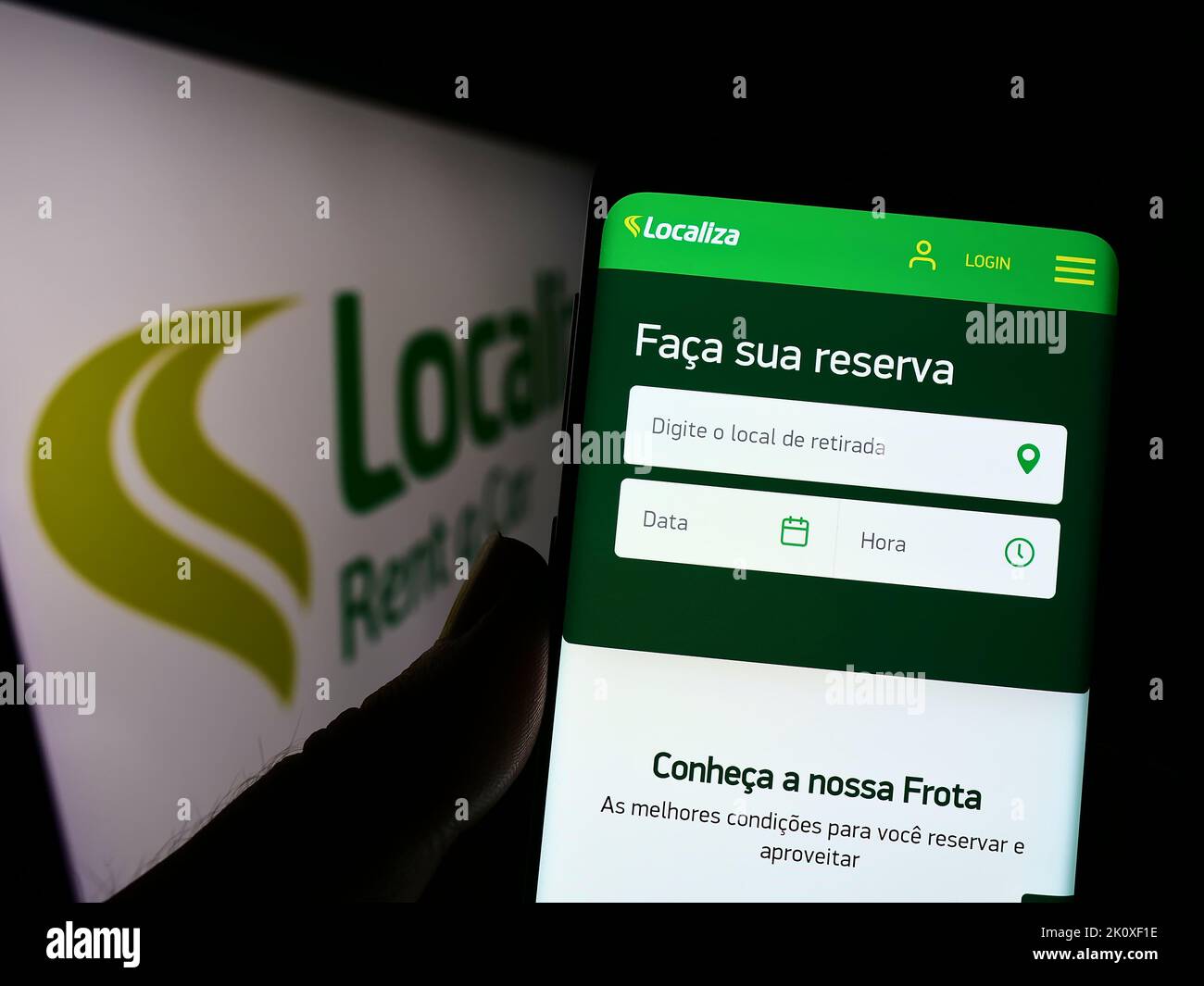 Person holding smartphone with webpage of Brazilian company Localiza Rent a Car S.A. on screen in front of logo. Focus on center of phone display. Stock Photo