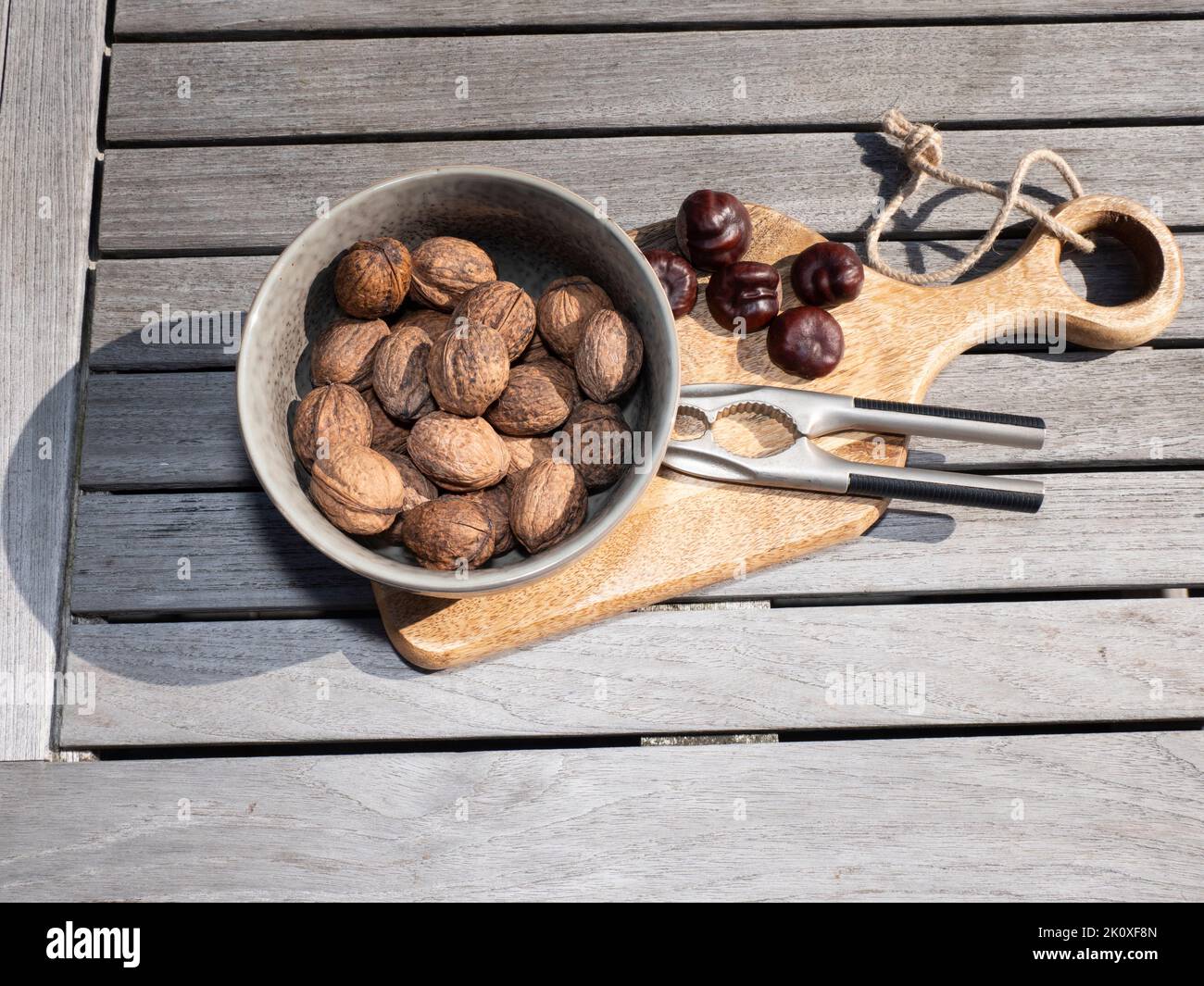 Walnuts in a bowl and chestnuts on a wooden board with a nutcracker and a wooden table Stock Photo
