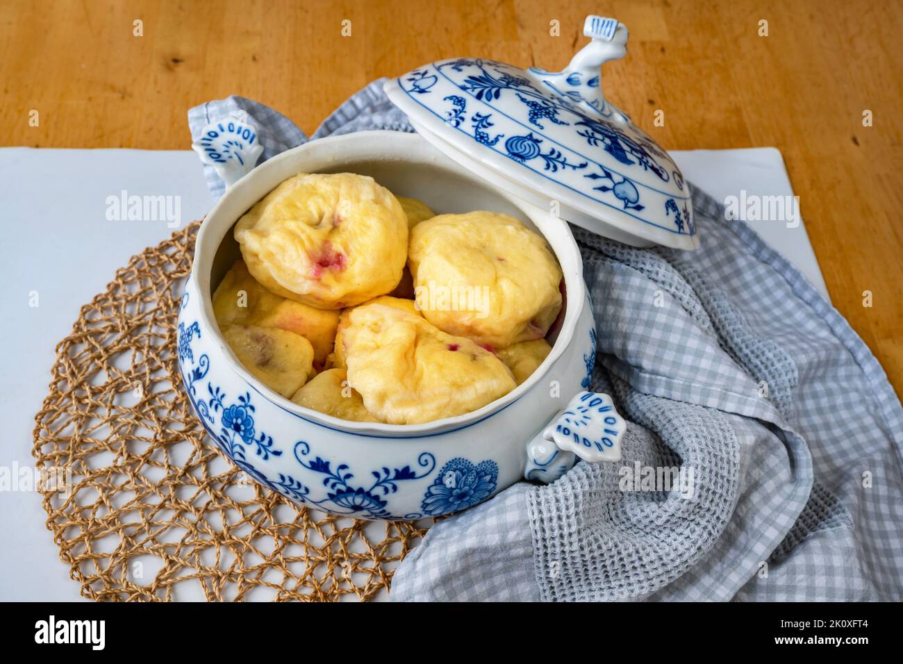 Boiled sweet plum dumpling in open decorative bowl with lid, towel, bamboo pad on table, closeup. Stock Photo