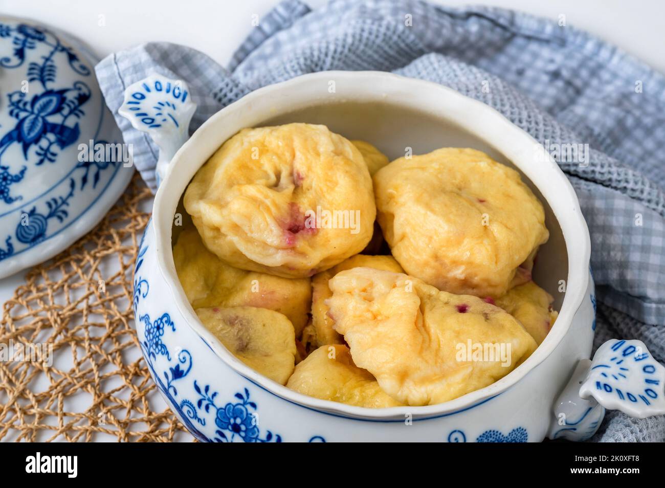 Boiled sweet plum dumpling in open decorative bowl, lid, towel, bamboo pad on table, closeup. Stock Photo