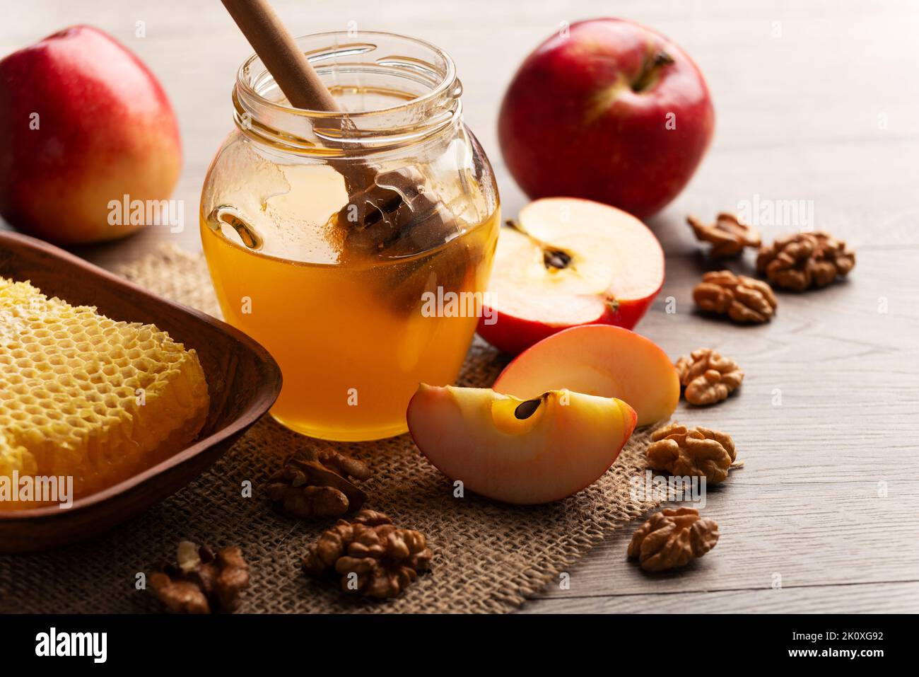 Mason jar with honey, honey dipper, honeycomb, red apples and walnuts on kitchen table Stock Photo