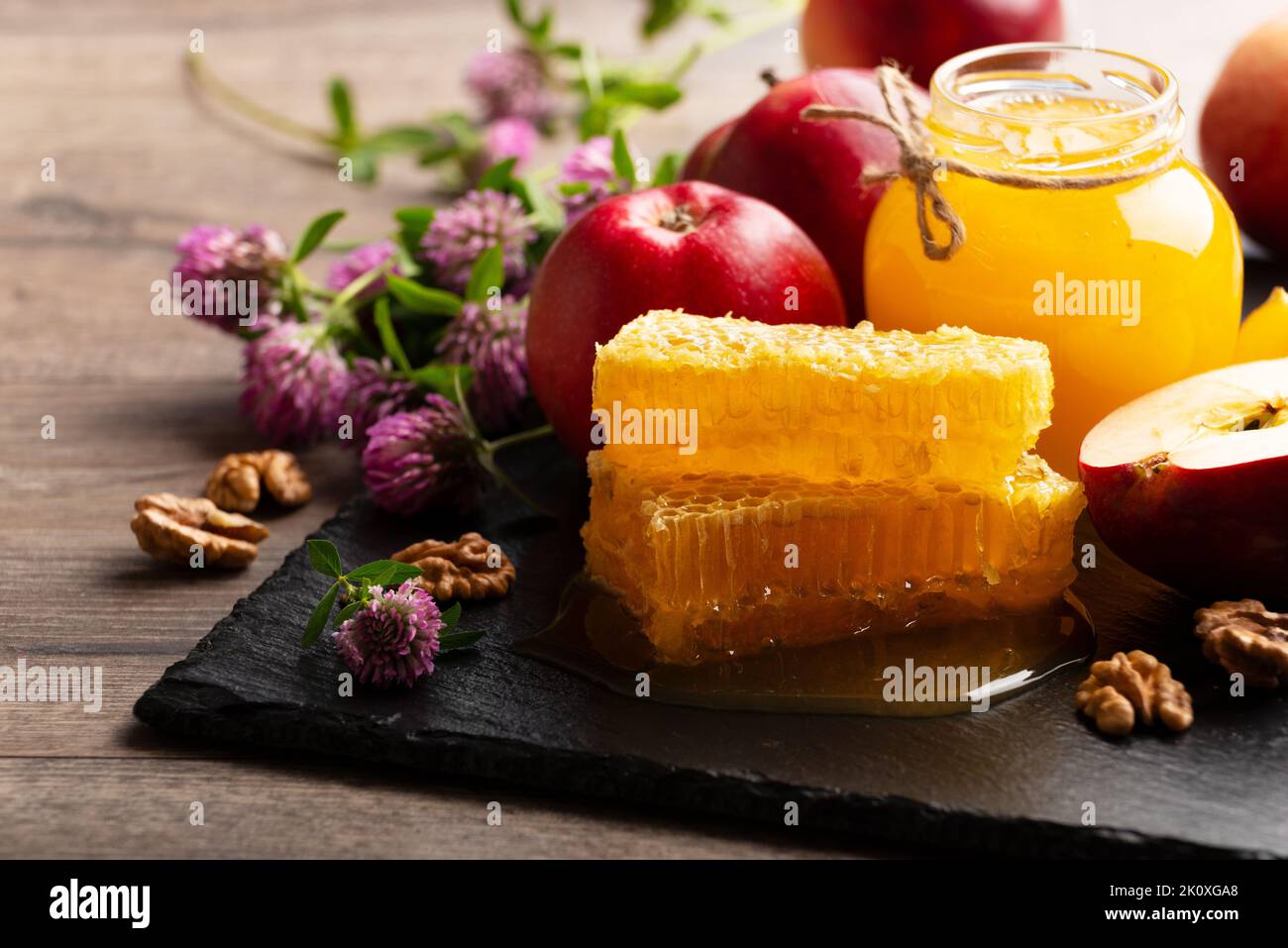 Mason jar with honey, honeycomb, red apples and walnuts on kitchen table Stock Photo