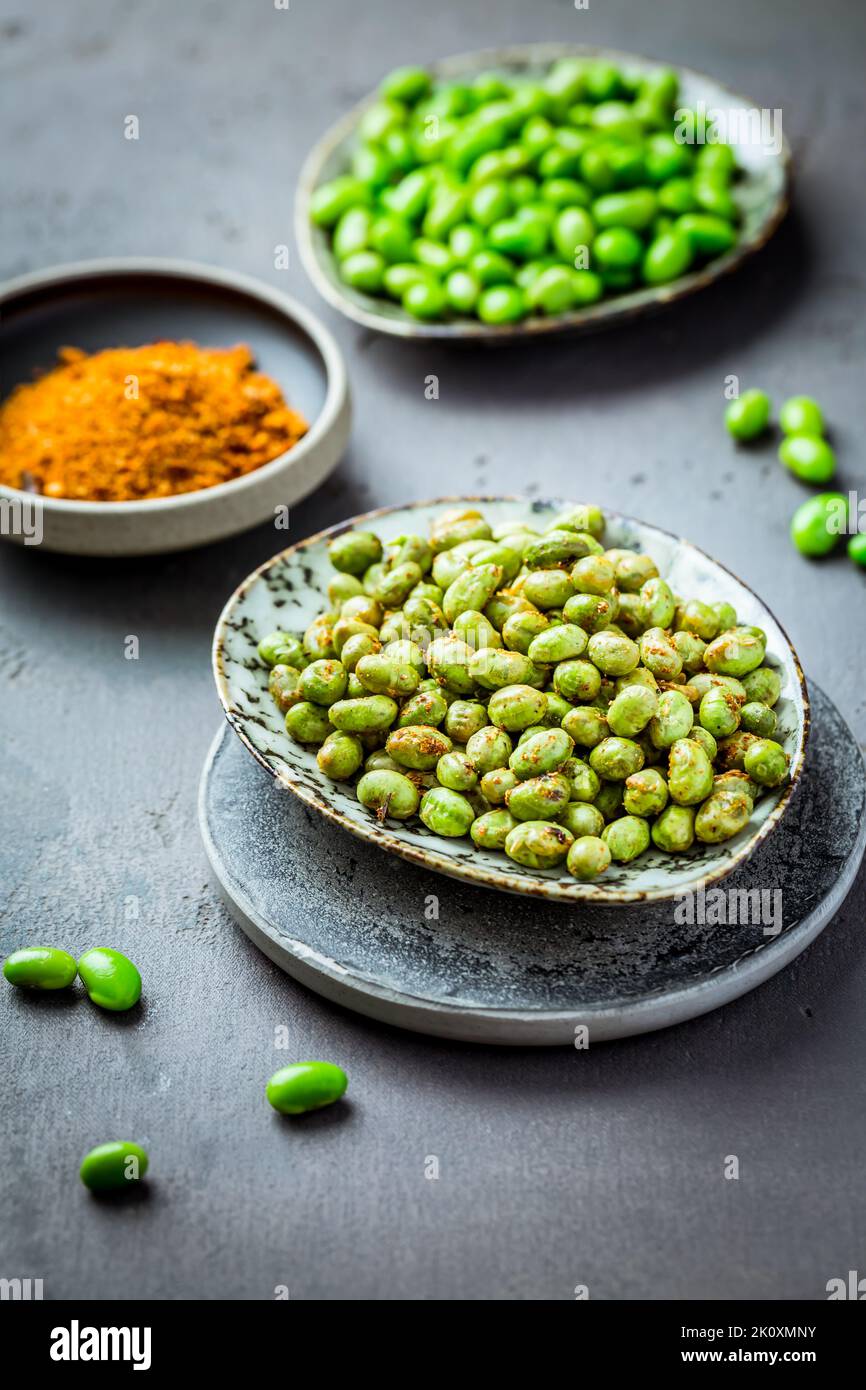 Roasted edamame beans as snack with spices and raw beans in background