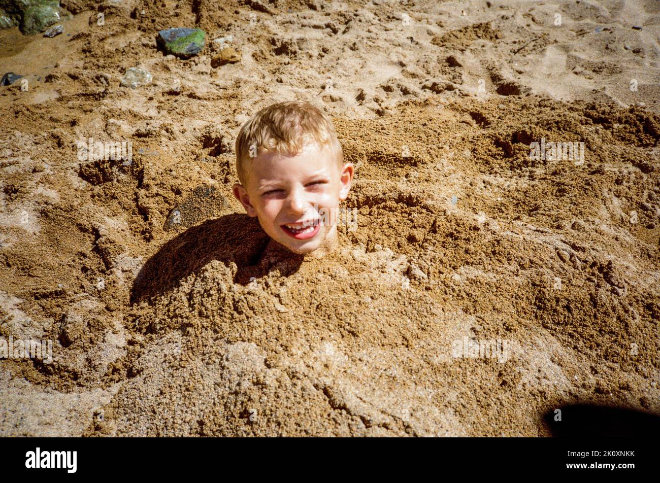 Five year old boy burried in the sand at Hope Cove Beach, Kingsbridge,Devon, England, United Kingdom. Stock Photo