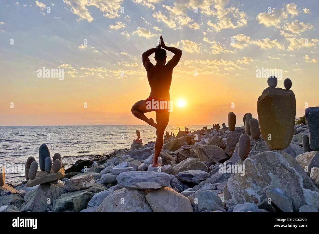 Lonely man in swimming trunks stands in a yoga pose on one leg. Rack on stones, other amazing levitate exposed with the center of gravity, balance. Wa Stock Photo