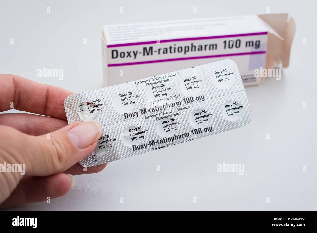 Woman taking Doxy-M-ratiopharm tablets by Ratiopharm for treating tick-borne borreliosis. Package of white pills. Pharmacy and medicine concept. Stock Photo