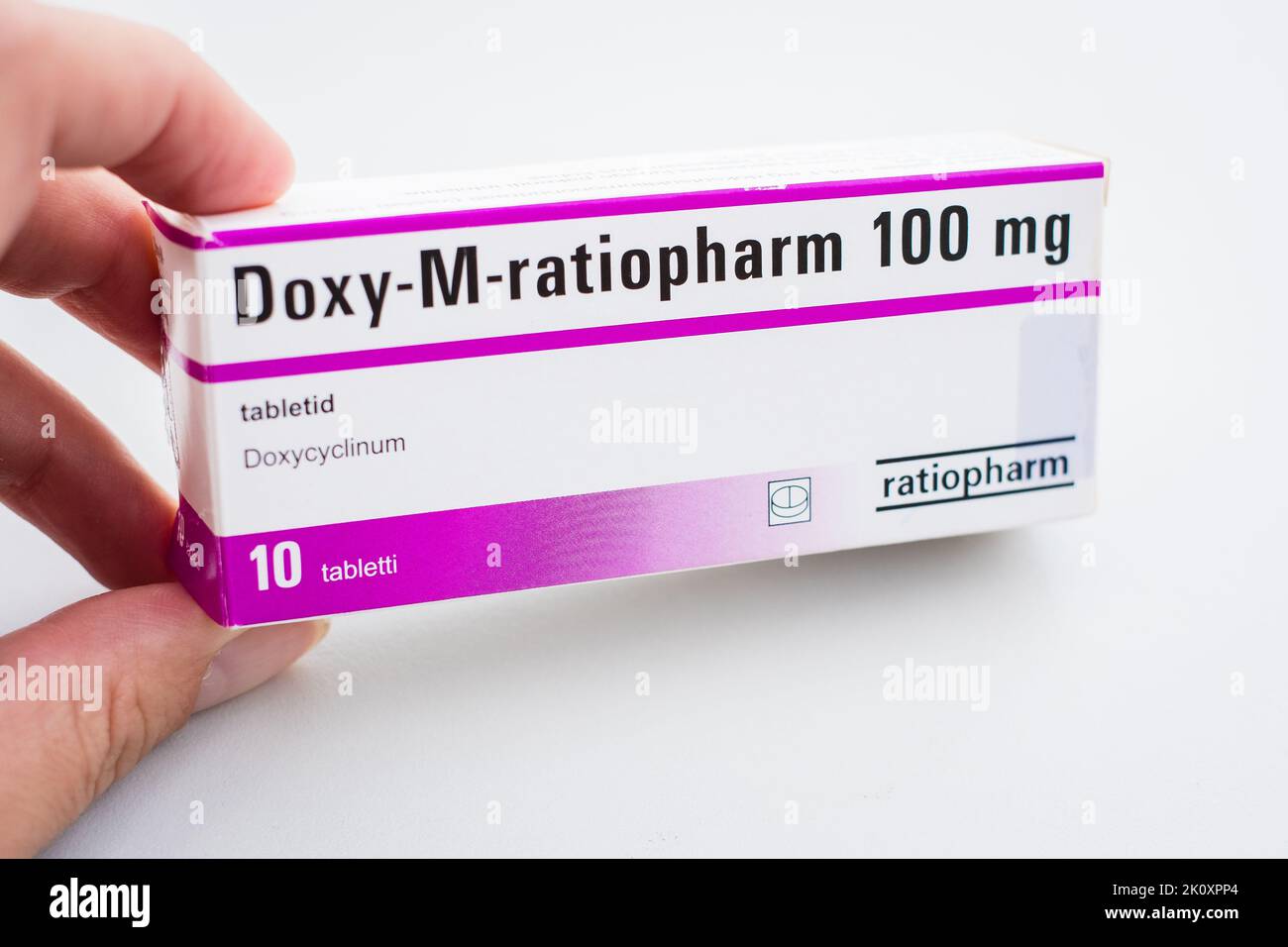 Woman taking Doxy-M-ratiopharm tablets by Ratiopharm for treating tick-borne borreliosis. Package of white pills. Pharmacy and medicine concept. Stock Photo
