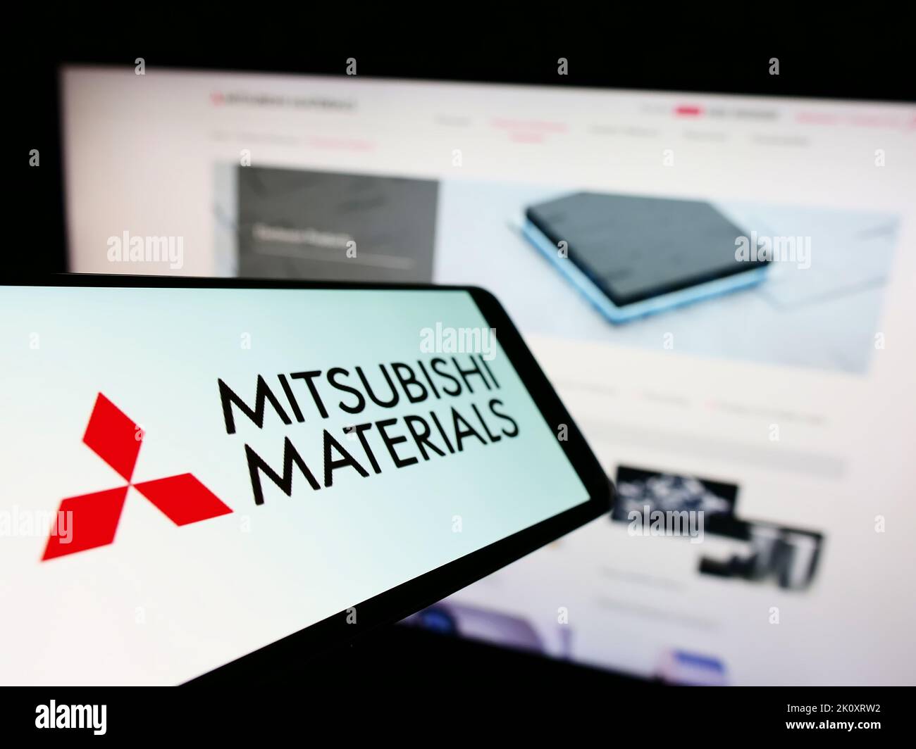Cellphone with logo of company Mitsubishi Materials Corporation (MMC) on screen in front of website. Focus on center-left of phone display. Stock Photo