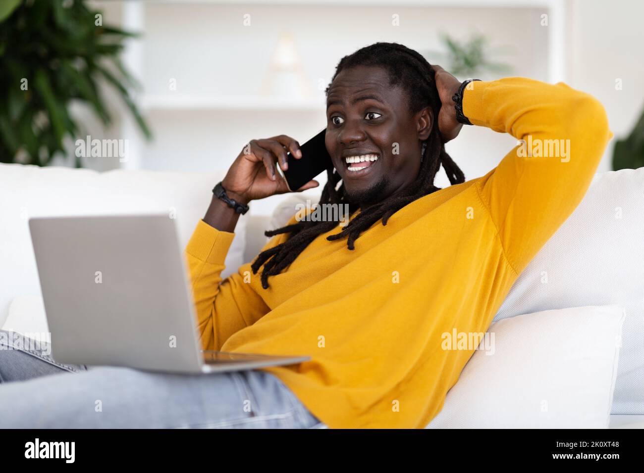 Excited Happy Black Man Talking On Cellphone And Using Laptop At Home Stock Photo
