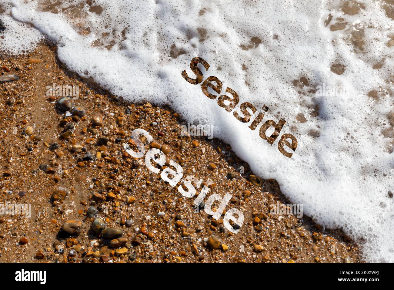 Seaside text cut out on both pebble beach and lapping waves  Stock Photo
