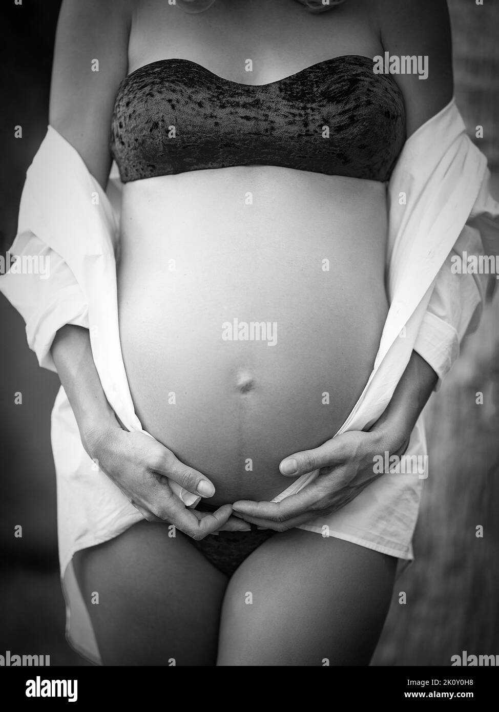 black and white image of mother's hands holding belly. Stock Photo