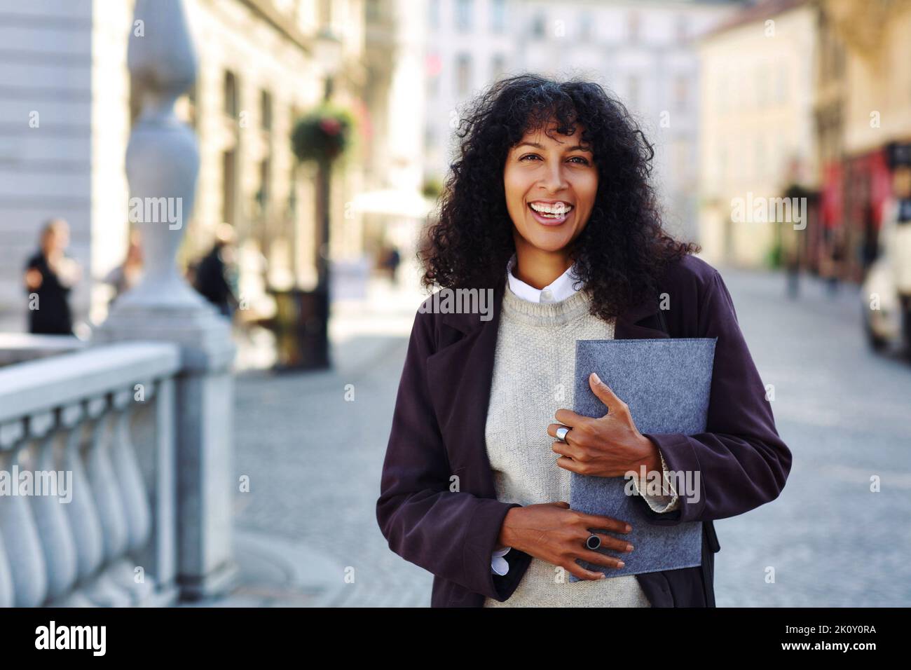positive businesswoman standing on street holding folder with documents curly black hair Stock Photo