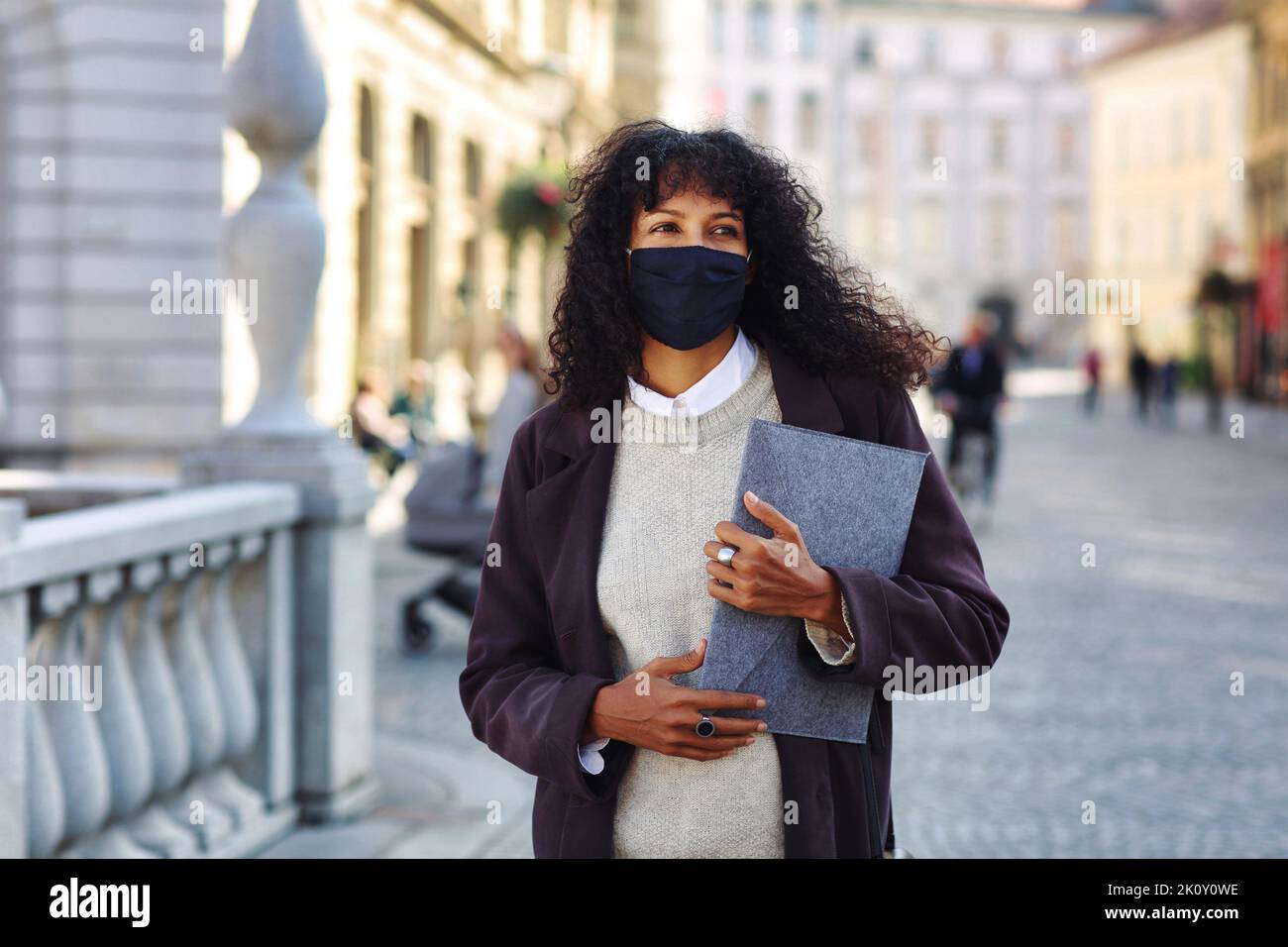businesswoman standing in street with face mask holding folder with documents Stock Photo