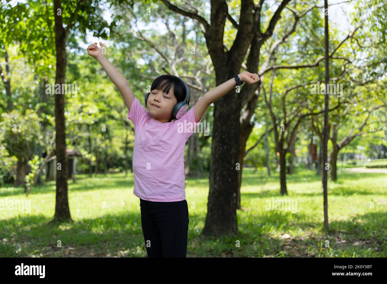 Portrait of child girl listens to music with modern headphones in park outdoors. Happy child enjoying rhythms in listening to music with headphones wi Stock Photo