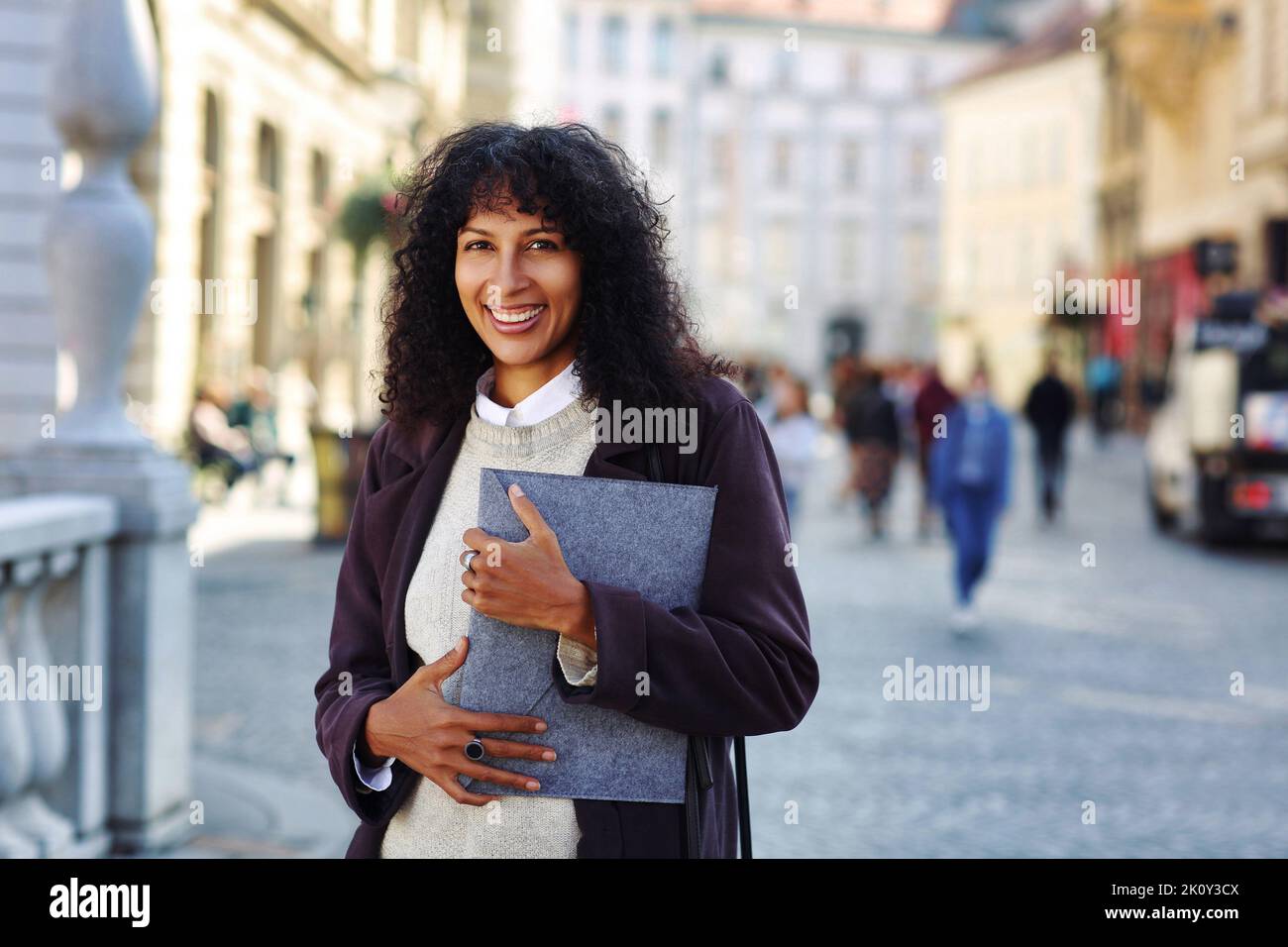 positive businesswoman standing on street holding folder with documents curly black hair Stock Photo