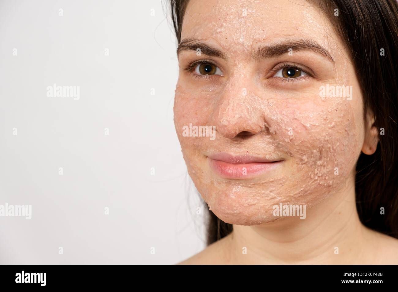 A young brunette woman makes cleansing facial treatments - a mask or scrub to cleanse and nourish the skin. Stock Photo