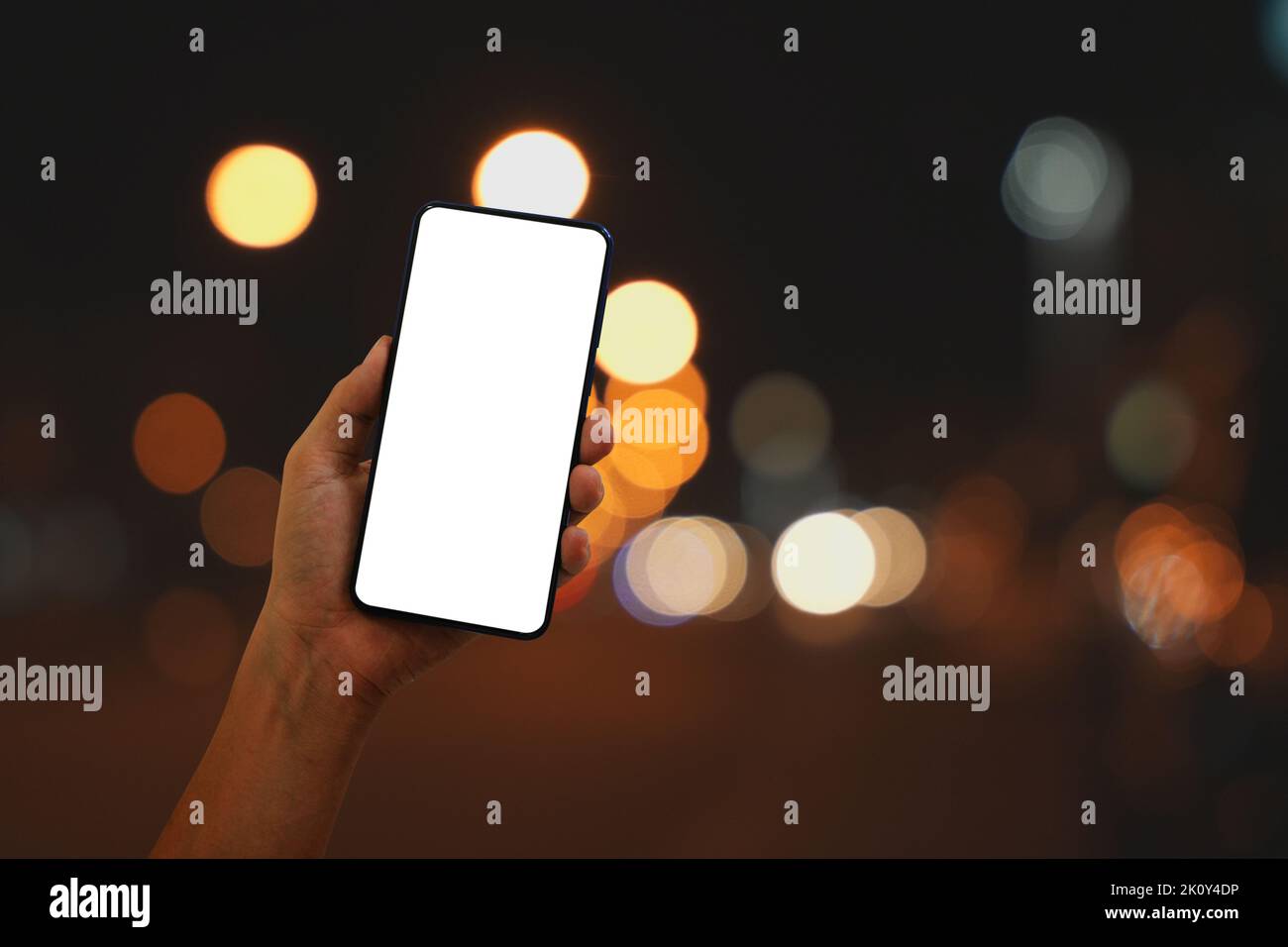 Hand holding smartphone with blank screen at night on bokeh city street ...