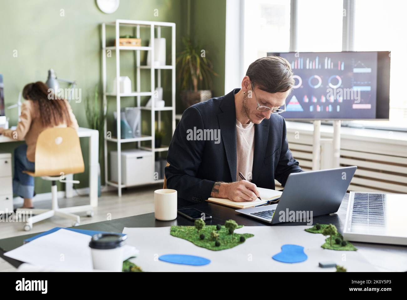 Young engineer making notes in notebook while working at his workplace with laptop at office Stock Photo