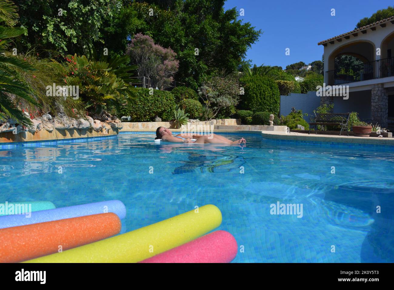 Young woman sunbathing and keeping cool, floating in swimming pool in a Mediterranean garden Stock Photo