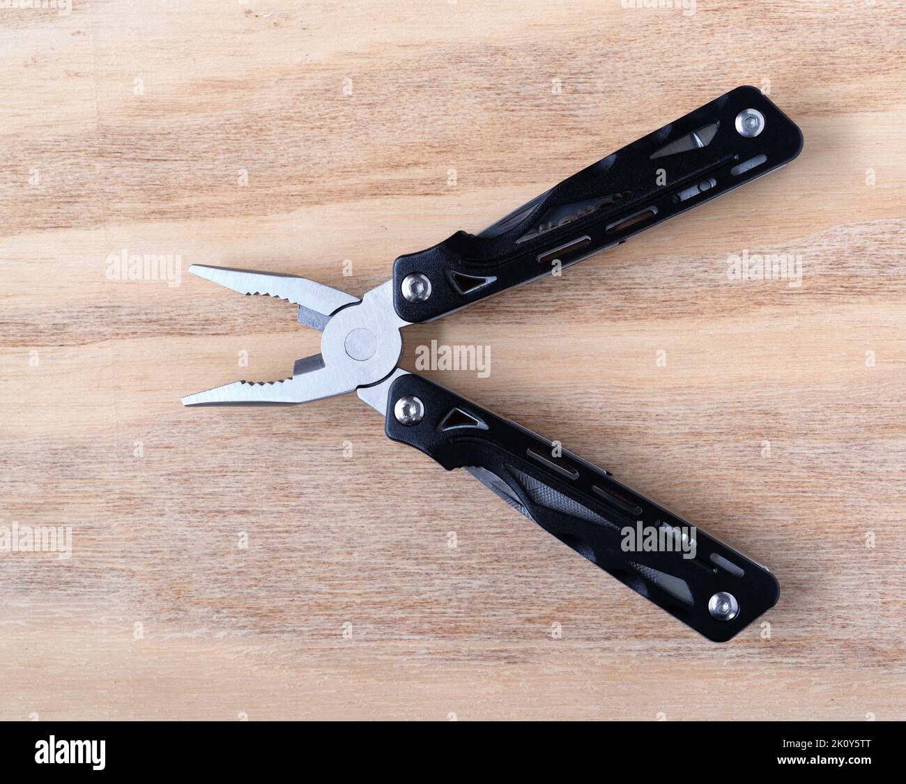 Top view of multi functional pliers open on a wood background top view. Stock Photo