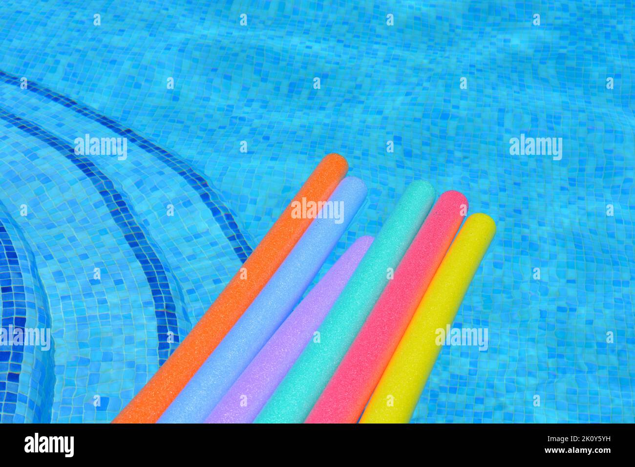 Rainbow coloured pool noodles floating on water in swimming pool Stock Photo