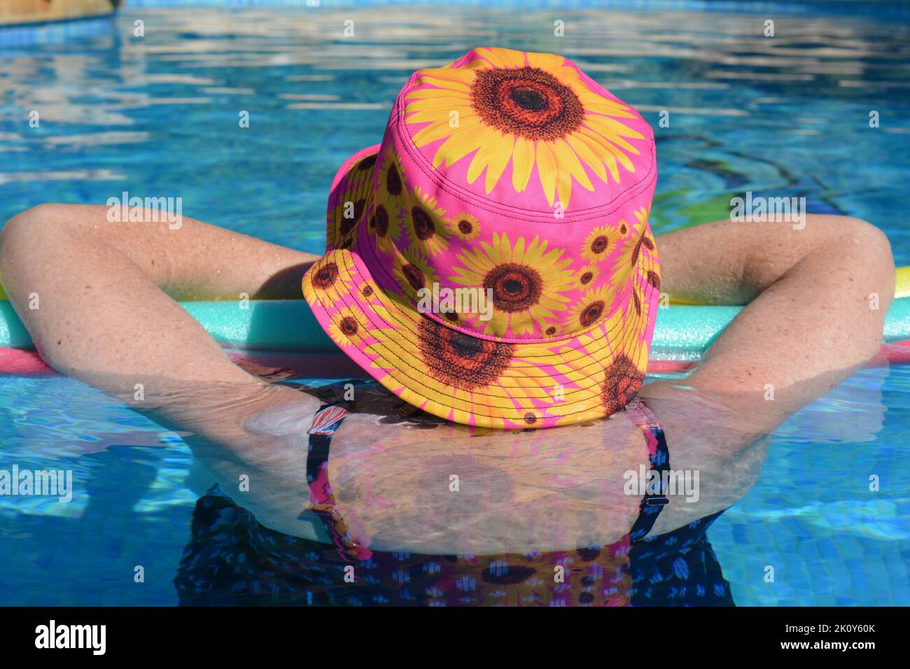 Woman from behind in swimming pool, wearing a sun hat with sun tan lotion on her shoulders Stock Photo