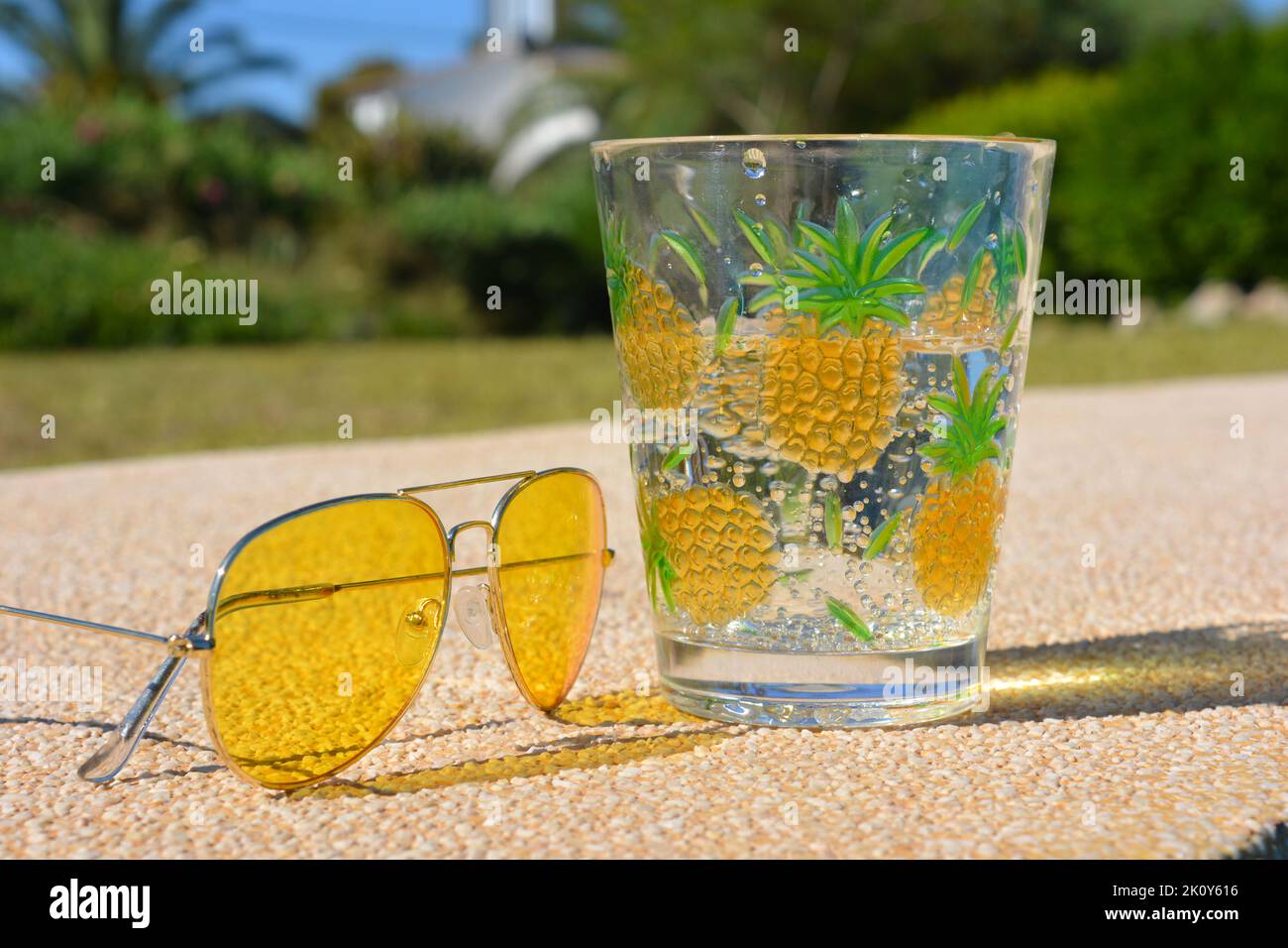 Yellow sunglasses next to a carbonated cold, clear drink outdoors Stock Photo