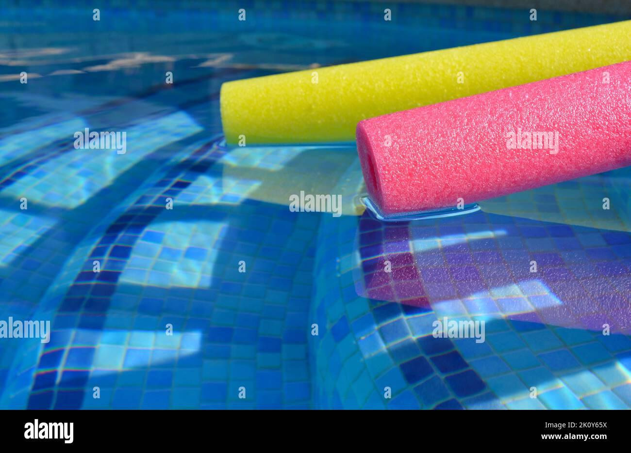 Swim noodles in blue tiled swimming pool, selective focus on pink polyethylene foam Stock Photo